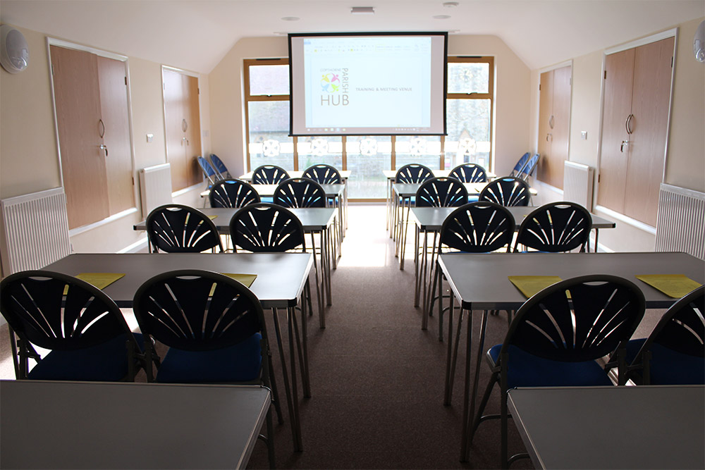 A large room with a windo takin gup the whole far wall with tables on both sides facing a projection board